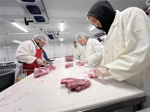 student scraping meat with HEB employee